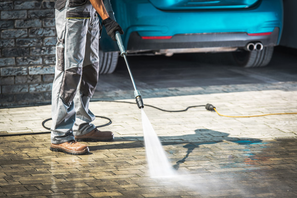 A man pressure washes his driveway to clean it.