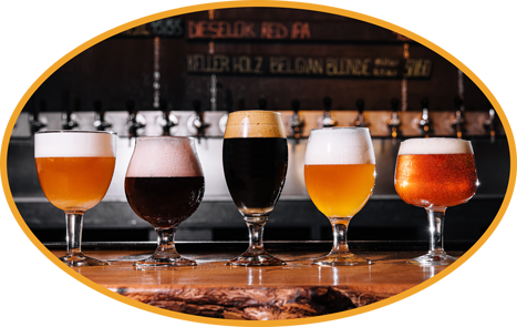 A variety of craft beers poured into their specific glasses sit atop a bar.