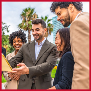 A group of business professionals gather to look at info about a chamber event on a tablet.